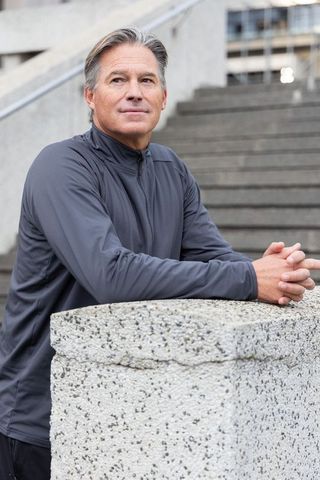 Senior man leaning on concrete post in urban plaza wearing gray jacket looking thoughtful
