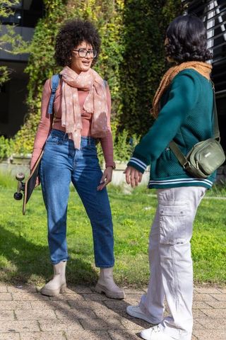 Young women chatting on campus path by vertical green wall carrying skateboard