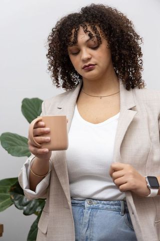 African american woman holding beige mug and adjusting blazer in modern minimalist home office