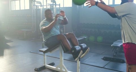 African american men training core with partnered medicine ball sit-ups on decline bench