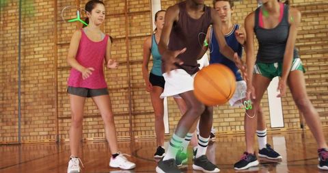Teen dribbling drill in school gym hardwood court with team practicing defense