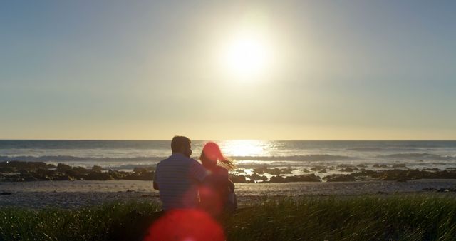 Rear view of romantic couple sitting at beach. Beautiful bright sun at beach 4k