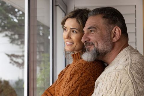 Mature couple gazing out window, sharing quiet moment in cozy knit sweaters