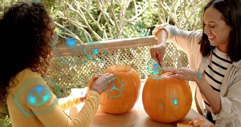 Two friends carving pumpkins on sunny porch together using hand tools for Halloween DIY decor
