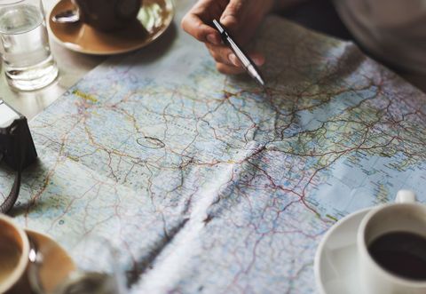 Hand Pointing at Map with Pen Planning Road Trip over Coffee