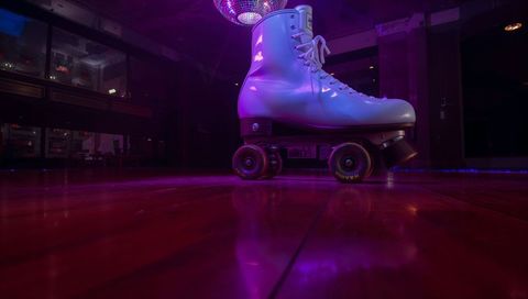 White roller skate resting on glossy neon rink with disco ball reflection and magenta glow