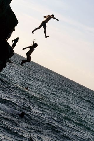 Joyful Moment of People Cliff Jumping into Sea