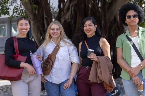 Multiracial students posing and smiling on campus plaza with coffee and reusable bottle
