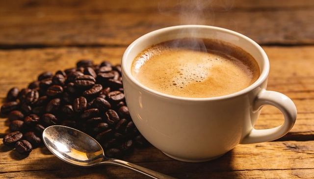 Steaming espresso cup on rustic wooden table with crema, roasted beans and spoon