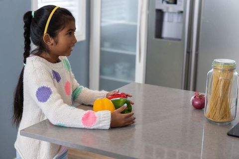 Indian girl holding colorful bell peppers at modern kitchen island for home cooking