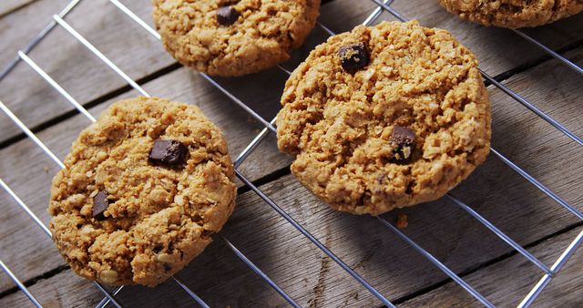 Freshly baked chocolate chip oatmeal cookies cool on a wire rack, with copy space. Their golden-brown texture and scattered chocolate chunks invite a moment of indulgent snacking.