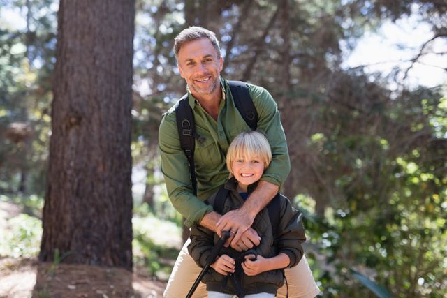 Portrait of happy father and son standing against trees in forest