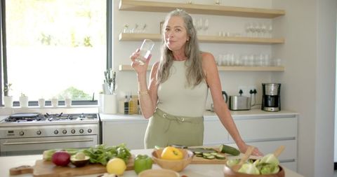 Mature Woman Drinking Water in Bright Modern Kitchen