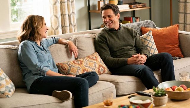 Couple chatting on gray sofa in sunlit living room with cozy pillows and coffee table