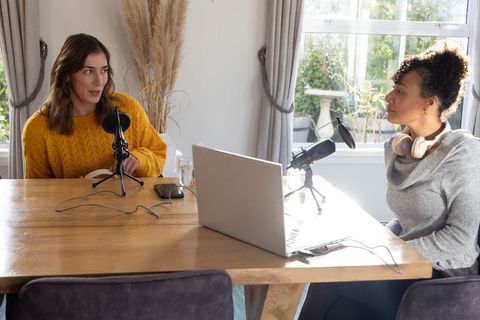 Diverse female co-hosts recording podcast conversation in cozy home studio with laptop