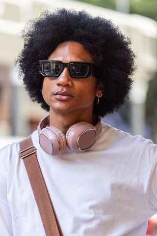 African american man standing on city street wearing sunglasses, pink headphones, white tee