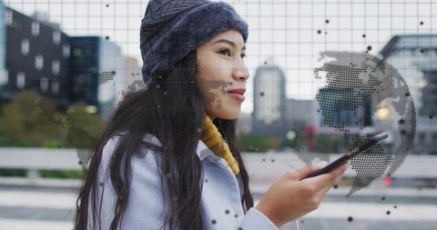 Young commuter holding smartphone wearing yellow scarf gazing ahead with digital globe overlay