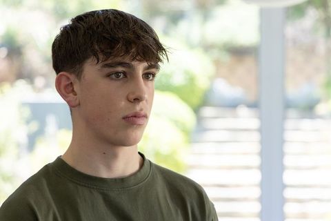 Teenage boy gazing through glass doors toward garden steps in serene daylight interior