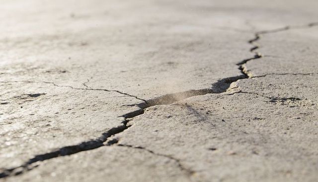 Sunlit cracked earth fissure on dry mud flat macro texture for drought and repair concept