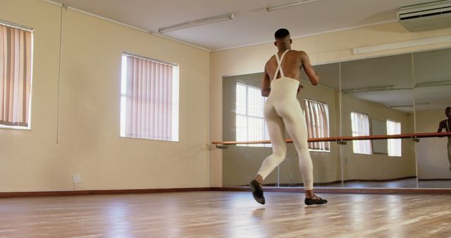 Male ballet dancer practicing in a spacious dance studio with mirrors. Ideal for use in articles or advertisements about ballet training, male dancers, performing arts, and physical fitness.