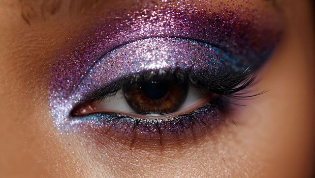 Close-up sparkling purple glitter eye makeup on female-presenting model with brown iris