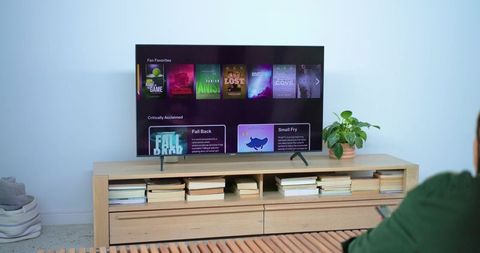 Man holding remote watching streaming interface on flat-screen tv in minimalist blue room