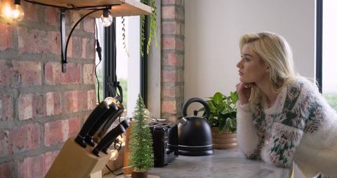Woman leaning on kitchen counter looking out window wearing fuzzy sweater cozy morning