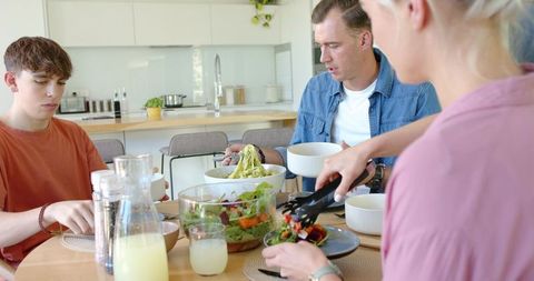 Family serving fresh salad and pasta at modern bright kitchen table for casual meal