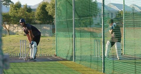 Adult batsman practicing in outdoor cricket nets wearing helmet and pads