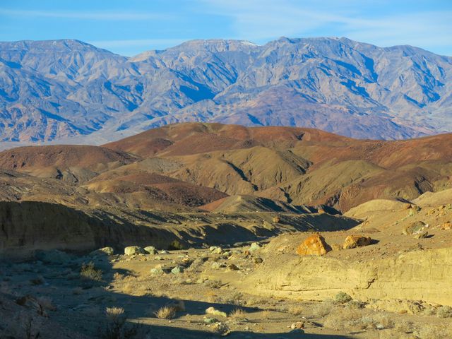 Rugged desert terrain with varying shades of brown and orange, presenting a beautiful contrast against mountain ranges in the background. Ideal for use in travel blogs, geological studies, outdoor adventure promotions, and nature documentaries.