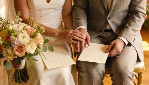 Bride and groom holding hands with handwritten vows and romantic bridal bouquet