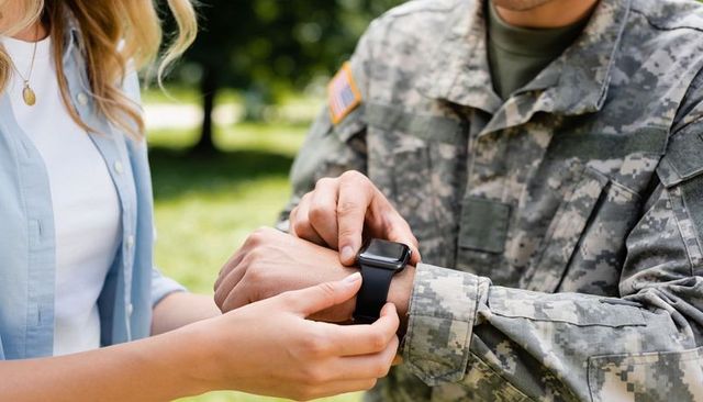 Civilian fastening smartwatch on soldier wrist outdoors with u.s. Flag patch