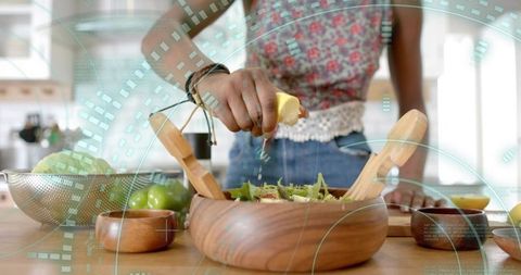Home cook squeezing lemon over fresh green salad in rustic kitchen
