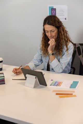Mature woman working on tablet with color swatches at modern creative desk for design project