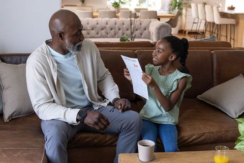African american grandfather celebrating granddaughter showing a+ report card on couch