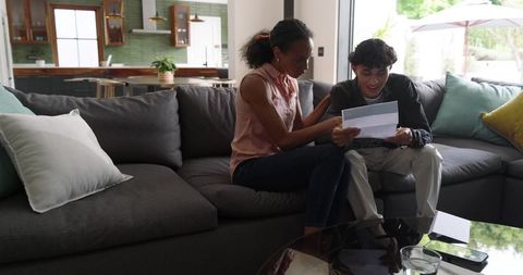 Diverse family reading joyful letter together on modern dark gray sectional sofa