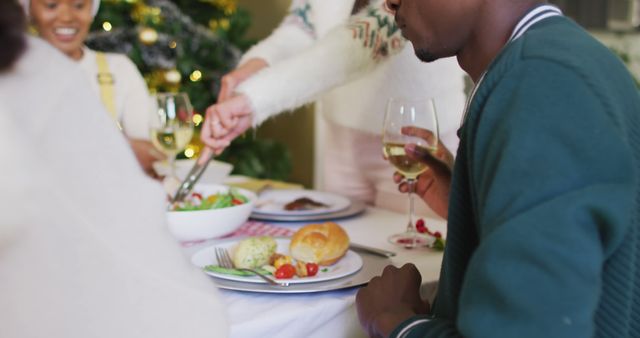 Picture showcasing a group of friends enjoying a Christmas dinner with dishes, wine, and cheerful interaction around a table. Christmas tree in the background adding to the festive ambiance. Ideal for illustrating holiday gatherings, festive celebrations, advertisements for holiday meals, and family-friendly content related to Christmas.