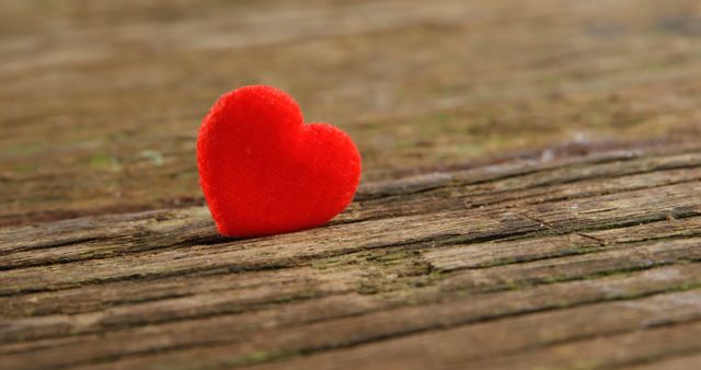 A small red heart rests on a textured wooden surface, symbolizing love and affection. It evokes emotions of romance and could be used for themes like Valentine's Day or expressing sentimental feelings.