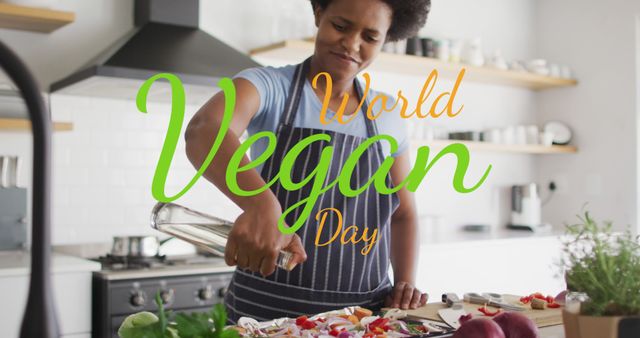 A man wearing an apron is celebrating World Vegan Day by preparing a colorful vegetable dish in a modern kitchen. This is perfect for use in promotional materials for vegan events, healthy eating campaigns, culinary websites, or lifestyle blogs focusing on plant-based diets.