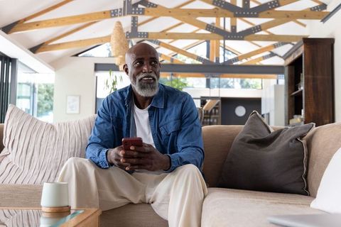 Mature african american man relaxing on sofa with smartphone in open-plan living room