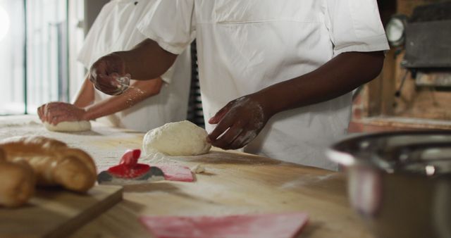 Chefs preparing dough on a wooden table, making artisanal bread. Useful for depicting bakery work, culinary arts, professional baking environment. Ideal for use in articles, blogs, and advertisements related to cooking, recipes, chef training, and food industry.