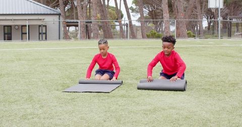 Young athletes unrolling mats on green turf field for outdoor exercise