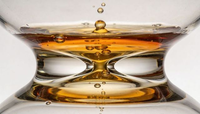 Macro of amber liquid reflecting in curved glass vessel with falling droplet and bubbles