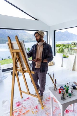 Asian artist painting at easel in bright coastal studio with seascape view