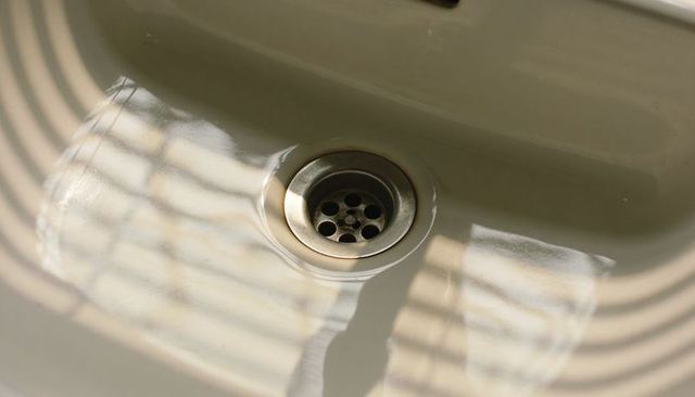 Off-white ceramic sink with chrome drain casting blinds stripes and soft light reflection