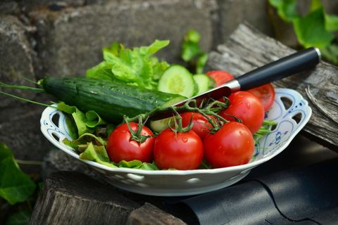 Plump vine tomatoes and cucumber resting on vintage bowl with leafy salad and knife