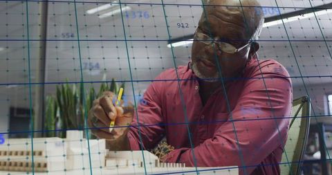Senior architect examining scale model with pencil over blueprint grid in studio