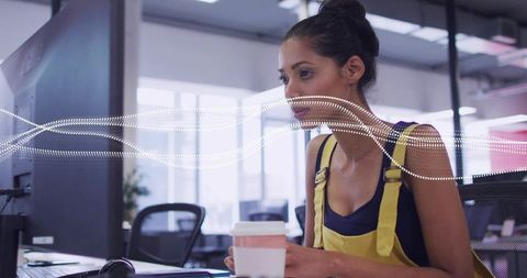 Young professional woman wearing yellow overalls focusing at computer in coworking space
