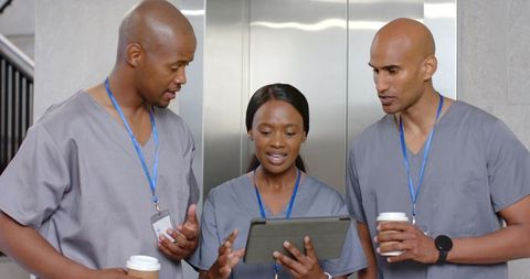 African american healthcare team reviewing tablet and drinking coffee in hospital corridor