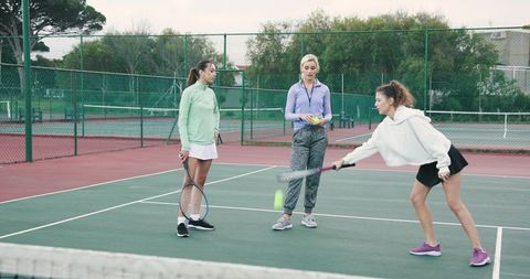 Female coach instructing young players during tennis drill on outdoor court overcast